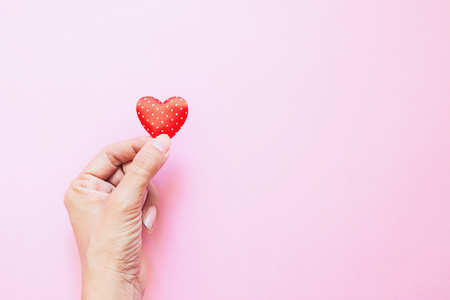 Girl's hand with mini polka dots red heart on pink background with copy space. Valentine's Day. Heart donation. Love conceptの写真素材