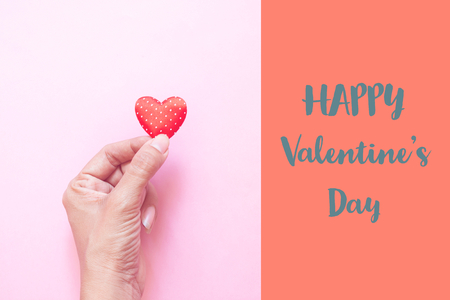 Woman's hand holding mini polka dots heart on pink colour background. Happy Valentine's Day conceptの写真素材