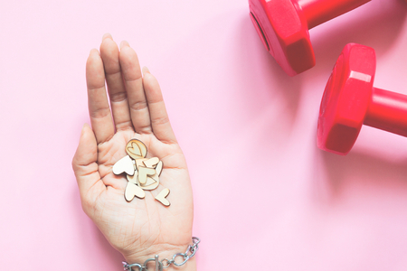 Woman's hand holding mini hearts and dumbbells on pink background. Health and Insuranceの写真素材