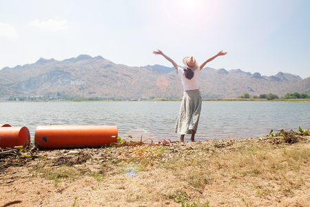 Happy asian woman in casual style clothing raised up arms and standing in the river with mountain view on background