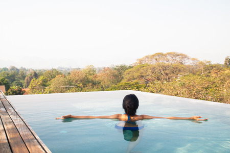 Asian woman swimming and relaxing in swimming pool on roof topの写真素材