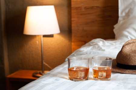 Two glasses of whiskey with ice on bed and lighting lamp in backgroundの写真素材