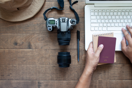 Overhead view of man hands using laptop and holding passport and camera on wooden backgroundの写真素材