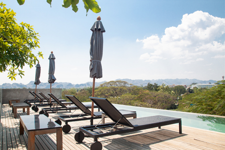 Kanchanaburi, Thailand - February 20, 2019 : Modern and simply design chaise lounge and swimming pool on the hotel roof top with mountain viewのeditorial素材