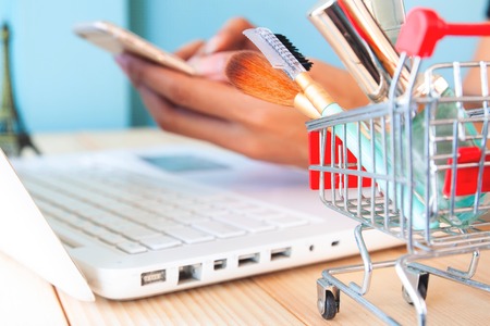Beauty items and cosmetics in shopping cart with woman shopping online on smartphoneの写真素材