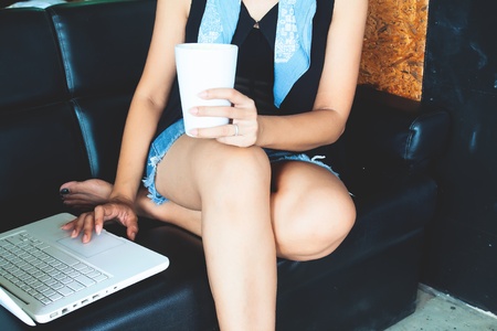 Woman in casual style clothing using laptop computer while drinking. Technology and lifestyle conceptの写真素材