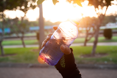 Close up sporty woman hand holding mineral water with sunset lightの写真素材