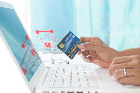 Hands holding credit card and using laptop computer with shopping cart background. Online shopping, E-payment or internet bankingの写真素材