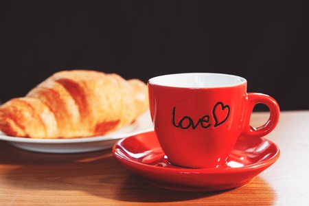 Red mug of coffee and croissant on wooden table, morning, love or healthy conceptの写真素材