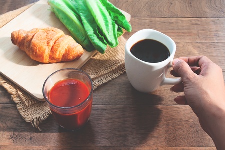 Woman hand holding black coffee cup with healthy breakfast on wooden table. Wellbeingの写真素材