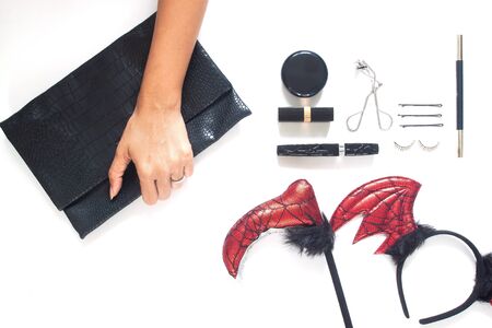 Woman hand holding trendy purse with Halloween party accessories and cosmetics on white background. Beauty Halloween conceptの写真素材