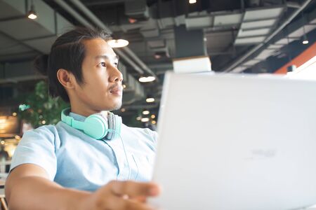 Handsome asian man using laptop looking out of window. Startup business conceptの写真素材
