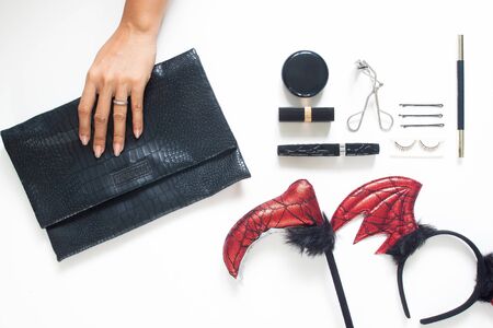 Creative flat lay of woman hand holding trendy purse with Halloween party accessories and cosmetics on white background. Beauty Halloween conceptの写真素材