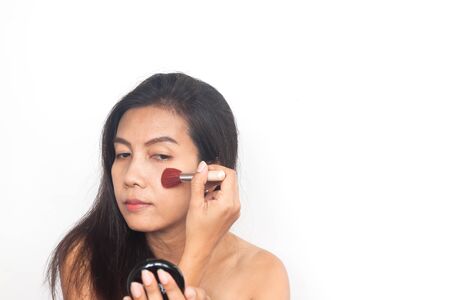 Portrait of 40s Asian woman applying brush on cheeks. Make up and Beauty concept. Anti aging and surgery.の写真素材