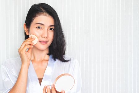 Facial Makeup. Beautiful Asian woman applying powder on faceの写真素材