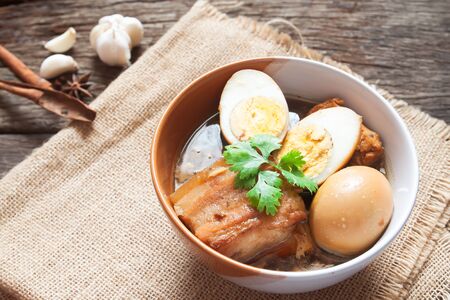 Stewed eggs and pork or eggs and pork in brown sauce in bowl with spices on wooden table. Top viewの写真素材