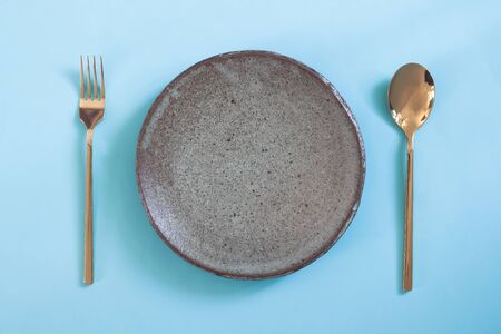 Empty plate, Table setting. Ceramic plate, spoon and fork on blue colour backgroundの写真素材