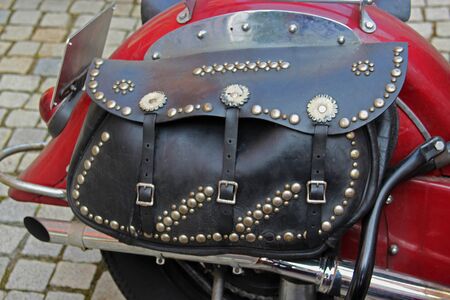 black leather bag with lots of rivets on an old red motorcycle, standing on pavementの写真素材