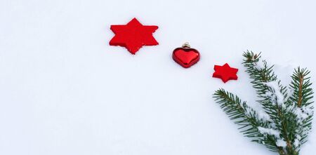 white and red Christmas background with felt stars, a heart pendant and a fir branch lying in snowの写真素材