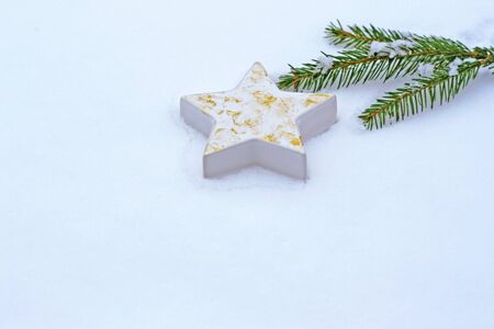 white porcelain Christmas star with gold powder and a fir branch lying in snowの写真素材