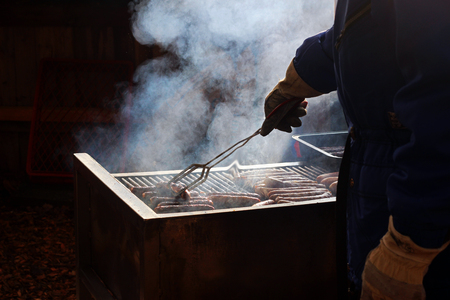 Sausages are served from an outdoor grill, man working with a barbecue tongの写真素材
