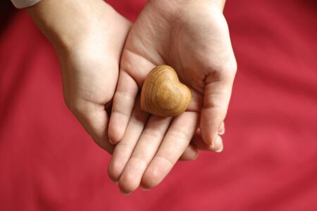 hands of a woman holding a wooden heart, bright red background