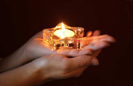 hands of a woman holding a lit tea light in star shape, low key, dark backgroundの写真素材