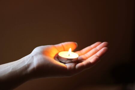 hand holding a lit tea light, dark backgroundの写真素材