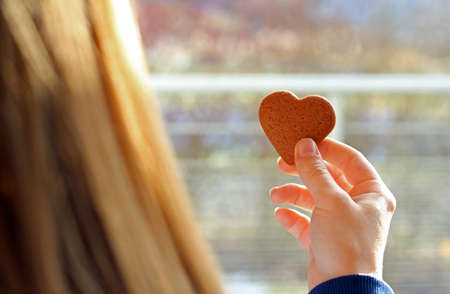 blond girl holding a heart cookie in her hand, backlit, rear viewの写真素材