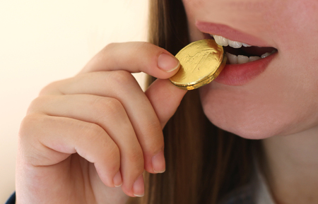 Girl with long hair biting in a gold coin coin, close-up, bright backgroundの写真素材