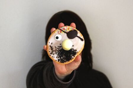 dark haired person with dark clothing holding a funny pirate face pastry in front of her faceの写真素材