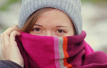 young woman outdoors in warm clothing, smiling, scarf drawn up into the faceの写真素材