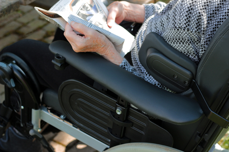 old person sitting outdoors in a wheelchair on a sunny day, reading a newspaperの写真素材