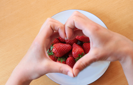 Hands forming a heart over a plate with strawberriesの写真素材