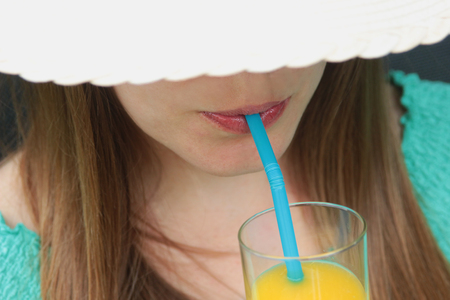 young woman with long brunette hair and a straw hat drinking orange juiceの写真素材