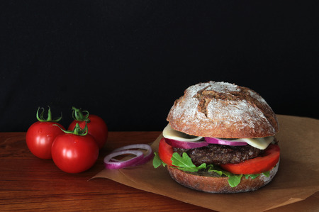 burger with a rye bun and cheese on wooden surface, black backgroundの写真素材
