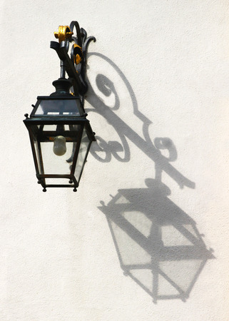 old-fashioned lantern, hanging on a wall in sunlight,  throwing its shadow on itの写真素材