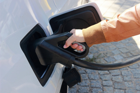 young woman with a leather jacket charging a white electric car
