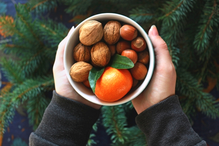 female hands holding a bowl with nuts and a satsuma over a table decorated with spruce branches, top viewの写真素材