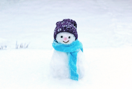 smiling little snowman with hat and scarf standing on a snow covered fieldの写真素材