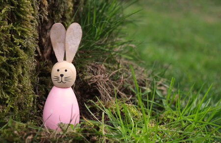 cute wooden Easter bunny standing in green grass beside a treeの写真素材