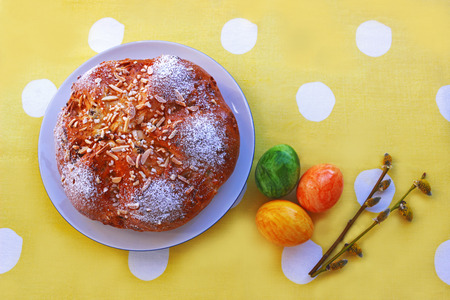 Easter bread, colored eggs and  willow catkins on a yellow tablecloth with white dots