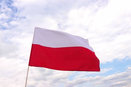 flag of Poland fluttering in the wind in front of blue and white skyの写真素材