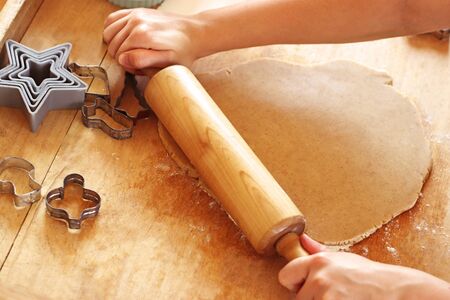 hands of a woman rolling out dough for christmas cookies on an old wooden board