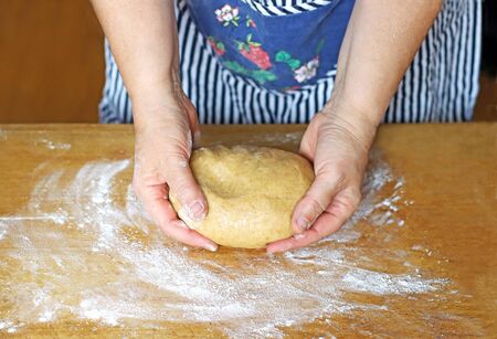 female hands holding a dough on an old wooden table, covered with flour