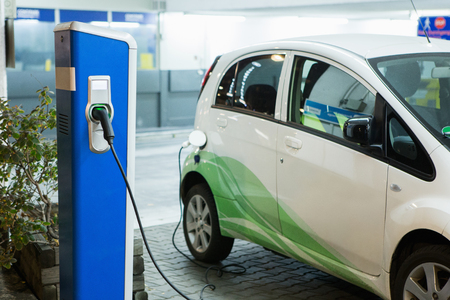 Electric car charged on a charging station in a indoor parking of shopping center by night.の写真素材