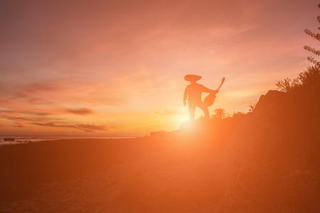 Mexican musician mariachi with a guitar. Silhouette on sunset background