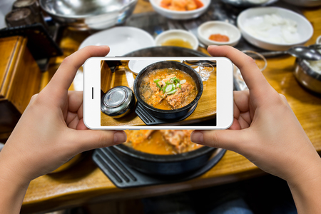A woman photographs a bowl of soup on the phone in the restaurant.の写真素材