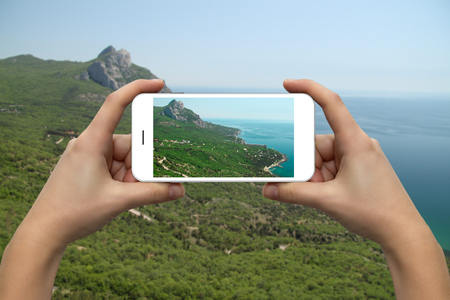 Female hands with a smartphone close-up. Photographing the coast of the sea and mountains.の写真素材
