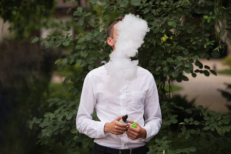 A man smokes an electronic cigarette. His face is covered with smokeの写真素材
